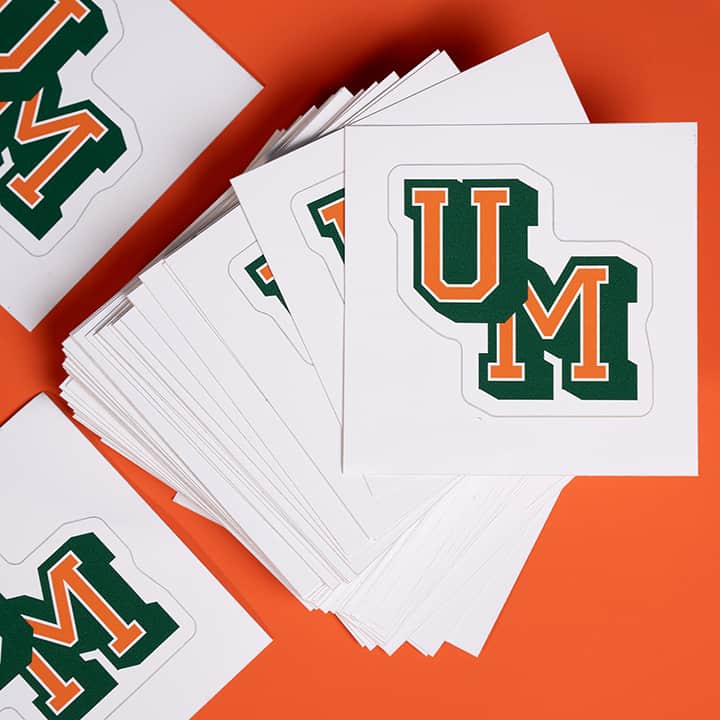 Stack of kiss cut stickers with 'UM' logo on an orange background