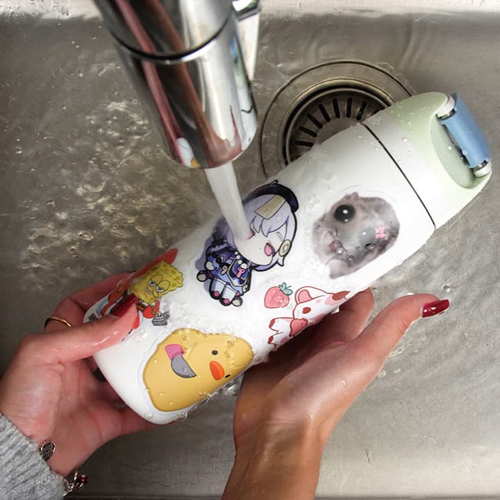 Person washing a thermos with cartoon designs under running water in a sink.