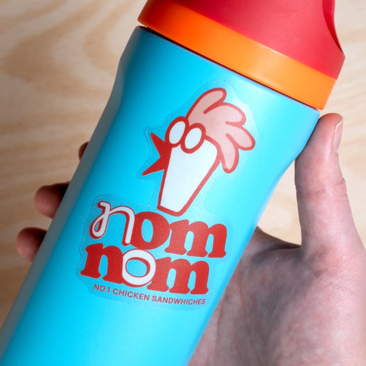 Blue cup with red lid featuring 'nom nom' logo and text on a wooden surface
