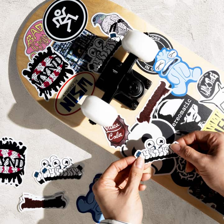 Skateboard with various stickers being held by a hand on a light background