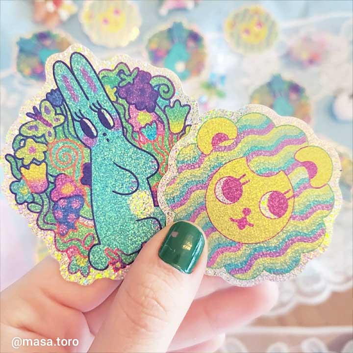 Colorful glittery stickers of a rabbit and a lion held by a hand with green nail polish.