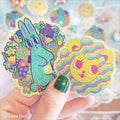 Colorful glittery stickers of a rabbit and a lion held by a hand with green nail polish.