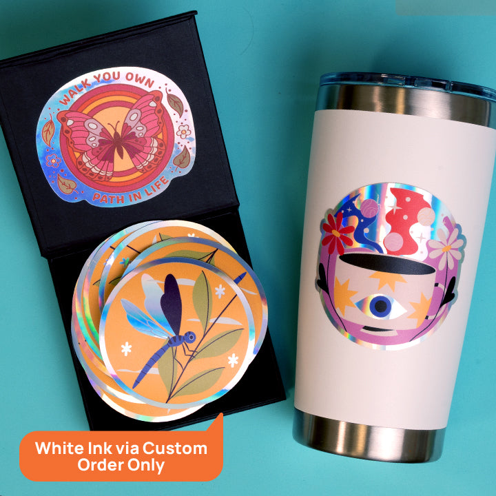 black box and white tumbler with colorful holographic stickers on them